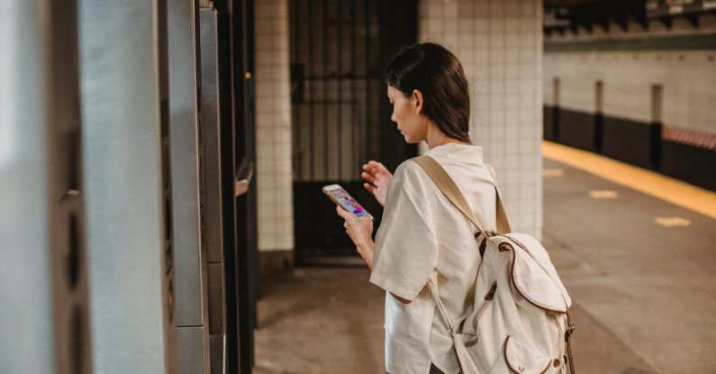 Online Platforms - Side view of young concentrated ethnic female in casual clothes and backpack browsing mobile phone while standing on platform of subway station